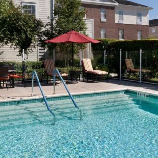 A tranquil outdoor pool area with lounge chairs and an umbrella on a sunny day.
