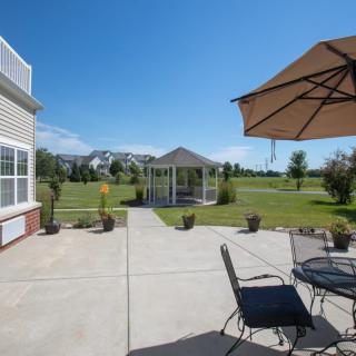 A sunny patio with outdoor furniture and a gazebo in the distance, surrounded by greenery.