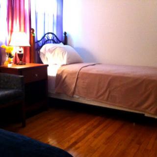 A cozy bedroom with a single bed, nightstand, and a lamp by the window.