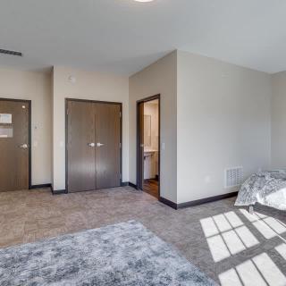 A spacious bedroom with carpet flooring, featuring doors and a window allowing natural light.