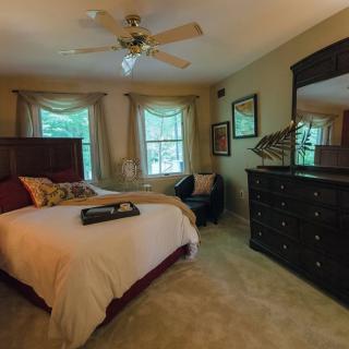 A cozy bedroom with elegant furniture, including a bed, dresser, and mirror, complemented by natural light from two windows.
