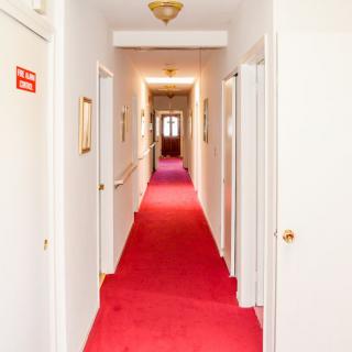 A narrow hallway with a red carpet, lined with doors on both sides and overhead lighting.