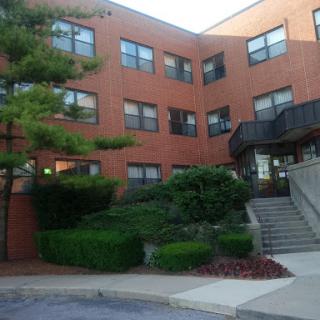 A brick apartment building featuring well-maintained landscaping and stair access.