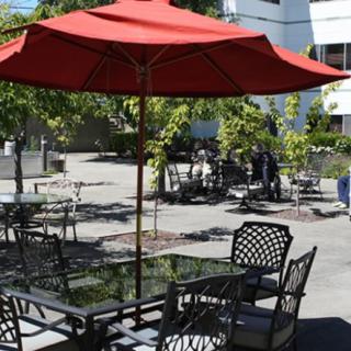 A sunny outdoor patio with tables, chairs, and a red umbrella.