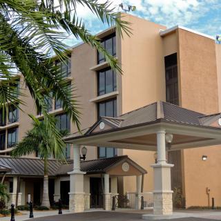 A modern hotel building with palm trees and a covered entrance.