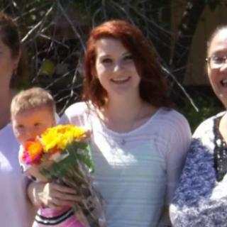 A group of people smiling outdoors, with one person holding a bouquet of flowers.