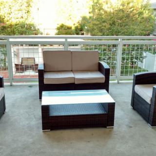 A cozy outdoor patio set on a balcony, featuring a loveseat, two chairs, and a coffee table.