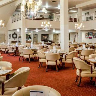 A spacious restaurant dining area with elegant chandeliers and neatly arranged tables and chairs.