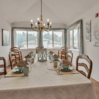 A beautifully set dining room with a large table, elegant chandelier, and ample natural light from surrounding windows.