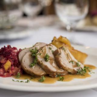 A gourmet plate featuring slices of chicken with sauce, accompanied by a side of vegetables.