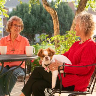 Two women enjoying a sunny afternoon with a dog and coffee.