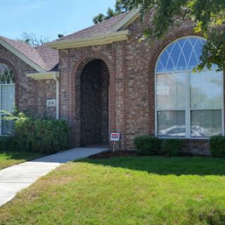 A charming brick house with large windows and a well-maintained lawn.