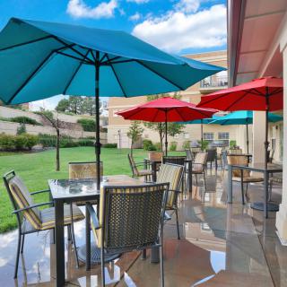 A sunny patio with colorful umbrellas and outdoor seating, overlooking a green lawn.