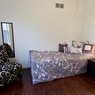 A minimalist bedroom with a single bed, decorative pillows, an armchair, and a mirror on the wall.