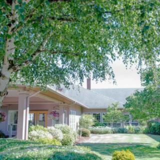A beautiful house surrounded by a lush, well-maintained garden and trees on a sunny day.