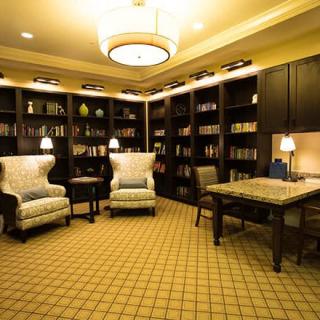 A cozy library room with bookshelves, armchairs, and warm lighting.