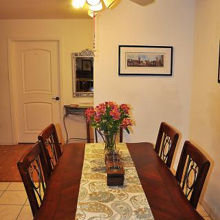A cozy dining room with a wooden table set, flowers in a vase, and decorative wall art.