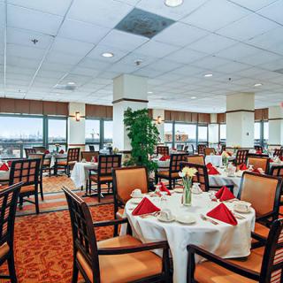 An elegant restaurant dining area with neatly arranged tables and chairs, featuring red napkins and a bright atmosphere.