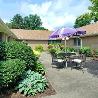 A tranquil patio area with outdoor furniture and a purple umbrella, surrounded by lush greenery.