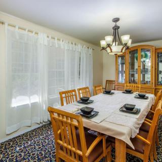 A cozy dining room with a wooden table set for six, complete with a decorative chandelier and sheer curtains.