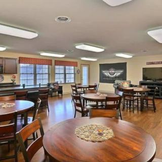 A well-lit community room with multiple tables and chairs, featuring a television and decorative elements.