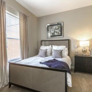 A modern bedroom with neutral tones, featuring a comfortable bed, decorative pillows, and a side table with a lamp.