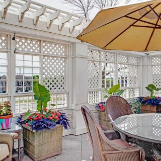 A cozy outdoor patio with a pergola, featuring a round table and chairs under an umbrella, surrounded by vibrant potted plants and flowers.