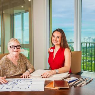 Two women engaged in a design meeting with plans and materials on the table, overlooking a scenic view.