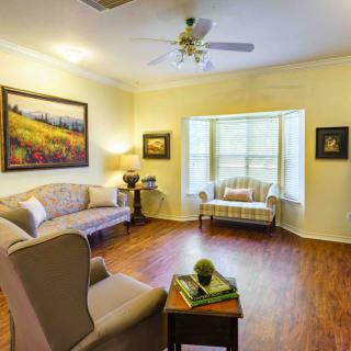 A cozy living room with elegant furniture and wooden flooring, featuring large windows and beautiful artwork.
