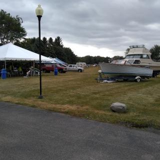 A recreational area featuring parked vehicles, a boat, and tents under a cloudy sky.