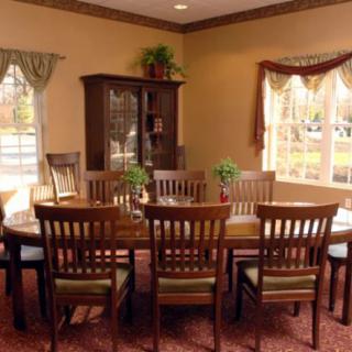 A cozy dining room with a wooden table and chairs, accompanied by a cabinet and large windows.