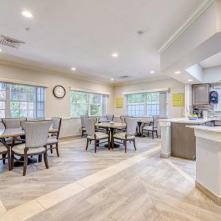 A spacious dining area with multiple tables and chairs, featuring large windows and a connected kitchen space.
