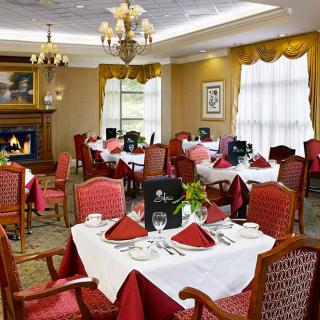 An elegant restaurant dining room with neatly set tables, red and white decor, and a cozy fireplace.