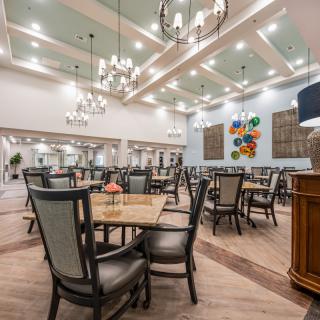 A spacious and elegantly designed dining room with multiple tables and chairs, adorned with chandeliers and decorative artwork on the walls.