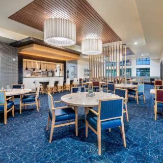 A modern restaurant interior with a dining area and bar, featuring blue carpeting and stylish lighting fixtures.