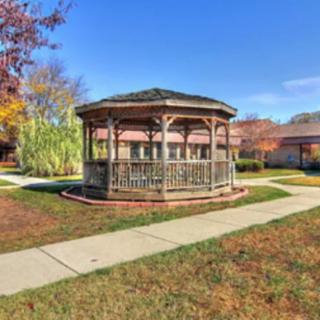A wooden gazebo surrounded by a well-maintained lawn and pathways on a clear autumn day.