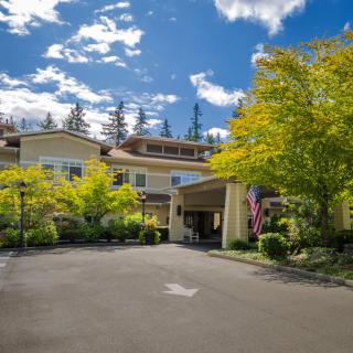 A welcoming entrance to a building surrounded by lush greenery under a partly cloudy sky.