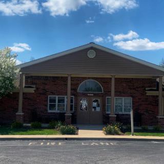 A brick building with a central entrance and a clear blue sky with clouds above.
