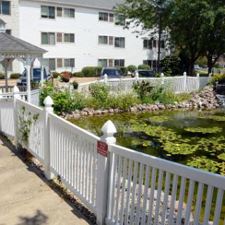 A serene garden featuring a pond, framed by a white picket fence in a residential setting.