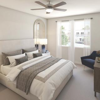 A modern and cozy bedroom with neutral tones, featuring a neatly made bed, ceiling fan, and natural light streaming through large windows.