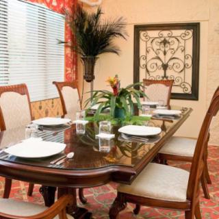 A well-decorated dining room with a polished wooden table set for a meal, surrounded by elegant chairs and adorned with plants.