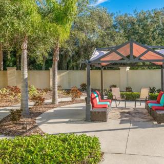 A sunny outdoor patio area with a gazebo, colorful seating, and lush landscaping.