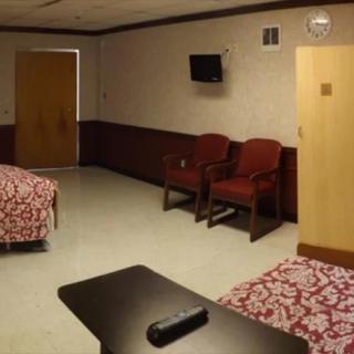 A hospital room with two beds, a TV, and chairs.