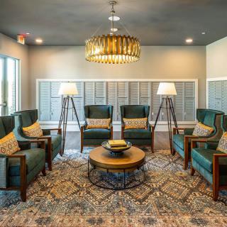 A stylish living room with green armchairs, a central coffee table, and elegant lighting.