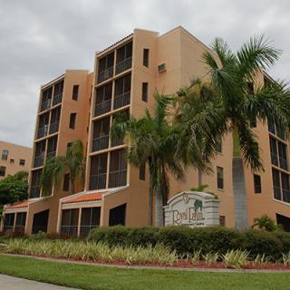 A modern apartment building with palm trees under a cloudy sky.