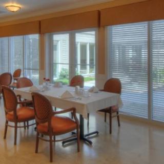 A well-lit dining room with a table and chairs, featuring large windows with blinds.
