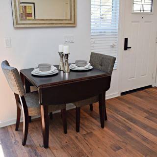 A cozy dining nook with a small table set for two, featuring elegant place settings and a wall mirror.