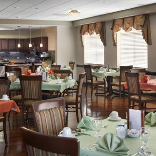A well-lit dining room with neatly arranged tables and chairs, set with green napkins and crockery.
