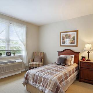 A cozy bedroom with a single bed, bedside table with a lamp, and a window with curtains.