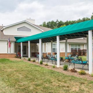 A building with a green canopy and outdoor seating area on a grassy lawn.